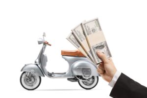 A young man in a suit holding stacks of U.S. dollar bills in his hand, with a silver vintage scooter in the background, isolated on a white background.