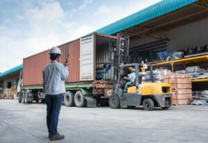 A team of warehouse laborers working together to unload goods using a forklift.