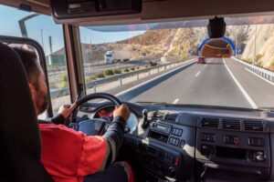 The image showing the view from inside the cab of a truck, with a driver on a highway approaching a tunnel entrance.